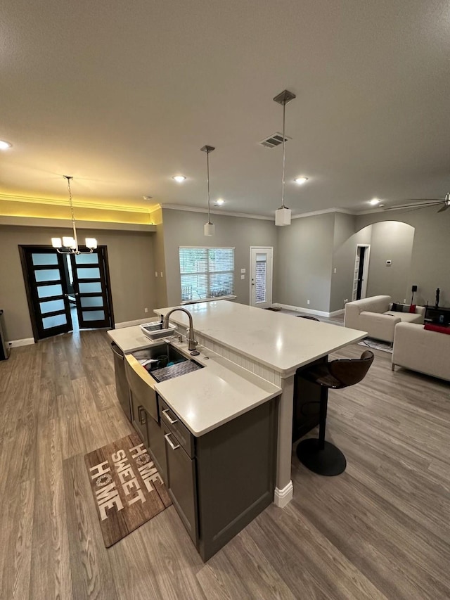 kitchen with sink, decorative light fixtures, hardwood / wood-style floors, a center island with sink, and a notable chandelier