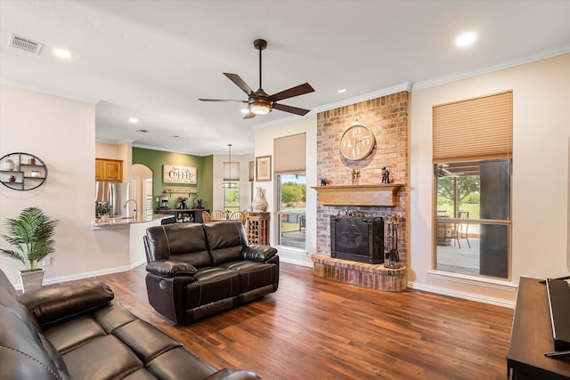 living room featuring a brick fireplace, crown molding, dark hardwood / wood-style flooring, and ceiling fan