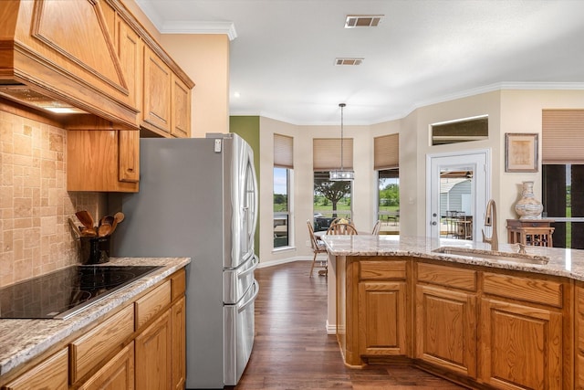 kitchen with premium range hood, light stone counters, black electric cooktop, decorative light fixtures, and sink