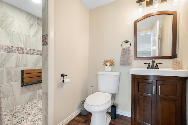 bathroom featuring toilet, hardwood / wood-style flooring, a tile shower, and vanity