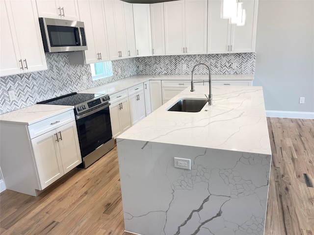 kitchen featuring light stone counters, sink, white cabinets, stainless steel appliances, and decorative light fixtures