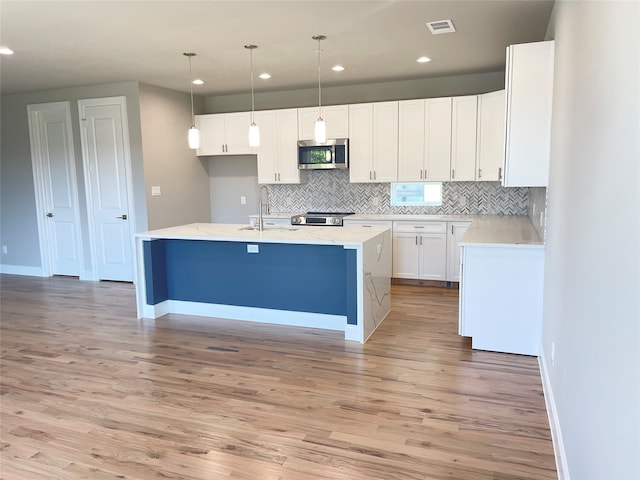 kitchen featuring an island with sink, decorative light fixtures, white cabinetry, appliances with stainless steel finishes, and light wood-type flooring