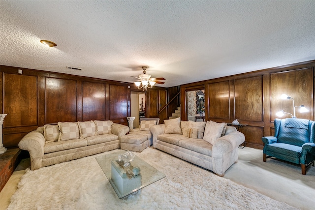 carpeted living room with ceiling fan, a textured ceiling, and wooden walls