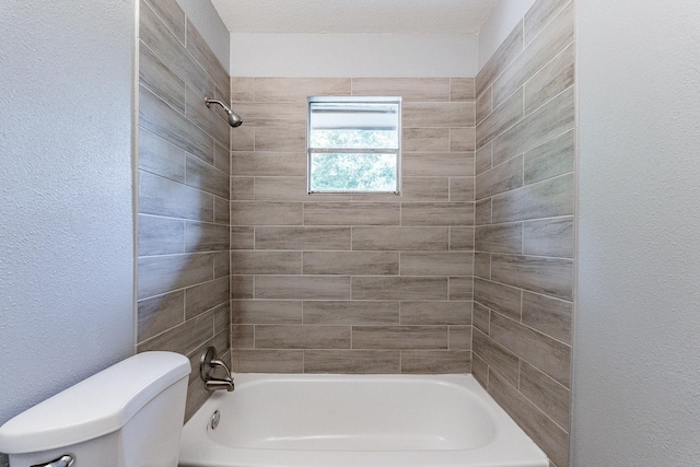 bathroom with a textured ceiling, tiled shower / bath combo, and toilet