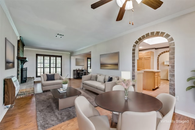 living room with a fireplace, light wood-type flooring, ceiling fan, and crown molding