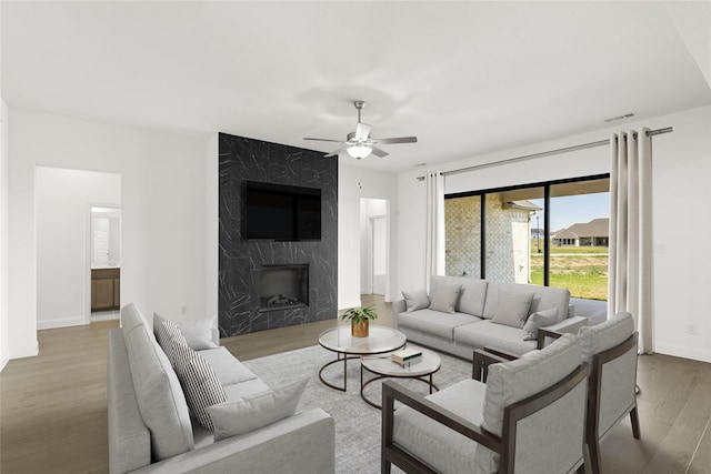 living room featuring ceiling fan, a fireplace, wood finished floors, visible vents, and baseboards