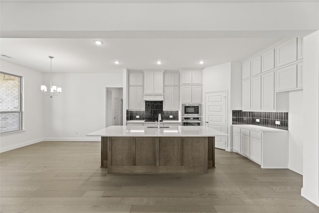 kitchen featuring oven, an island with sink, black microwave, light wood-type flooring, and white cabinets