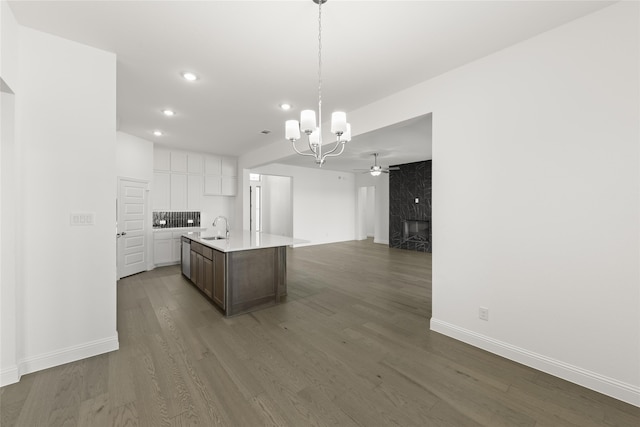 kitchen featuring a fireplace, ceiling fan with notable chandelier, white cabinetry, dark wood-type flooring, and a center island with sink