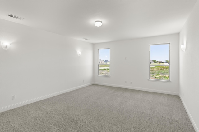 carpeted empty room with visible vents, baseboards, and a wealth of natural light