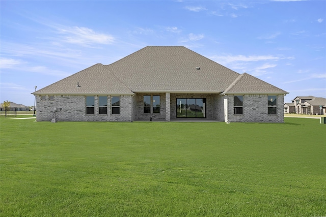 rear view of property featuring a shingled roof, a lawn, and brick siding