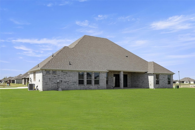 rear view of property with a yard, a shingled roof, brick siding, and central air condition unit