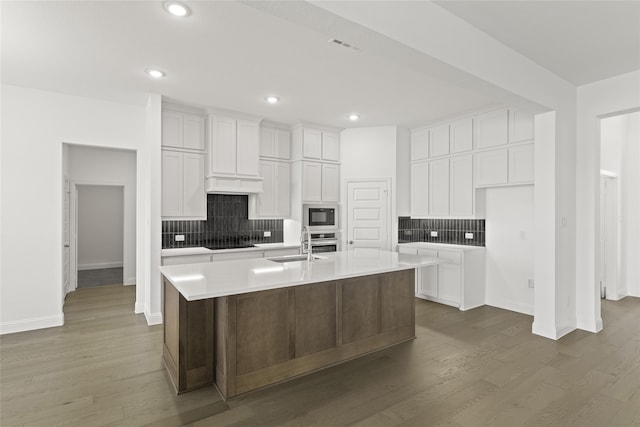 kitchen featuring dark wood-type flooring, a sink, white cabinets, black appliances, and an island with sink