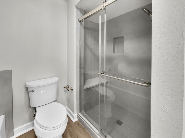 bathroom with toilet, a shower with door, and hardwood / wood-style floors