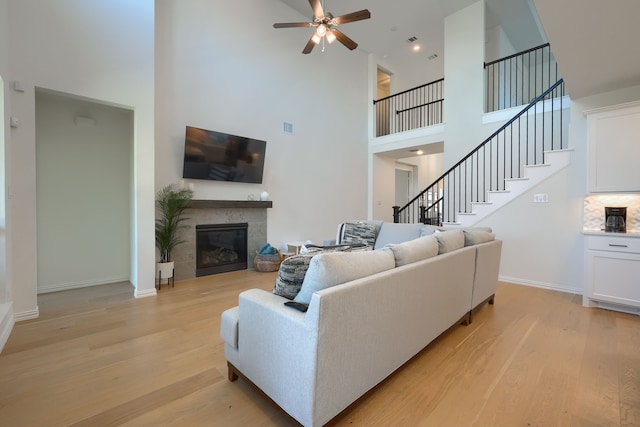 living room featuring a fireplace, a high ceiling, light hardwood / wood-style flooring, and ceiling fan