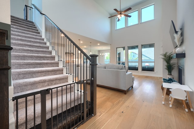 stairs with a high ceiling, ceiling fan, and wood-type flooring