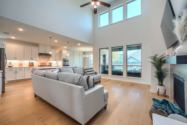 living room featuring sink, a towering ceiling, light hardwood / wood-style floors, and ceiling fan with notable chandelier