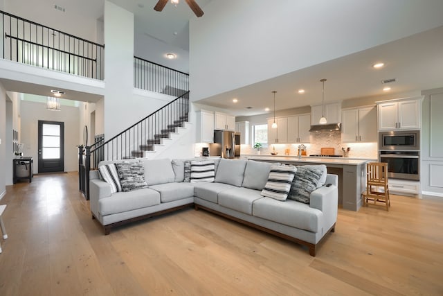 living room featuring a high ceiling, light hardwood / wood-style floors, and ceiling fan