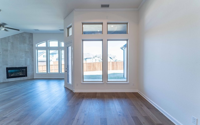 unfurnished living room with a healthy amount of sunlight, dark hardwood / wood-style flooring, a tiled fireplace, and ceiling fan