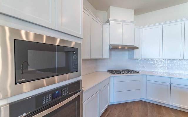 kitchen with stainless steel appliances, hardwood / wood-style flooring, tasteful backsplash, and white cabinetry