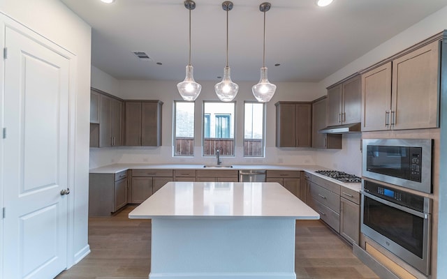 kitchen with decorative light fixtures, stainless steel appliances, a center island, wood-type flooring, and sink