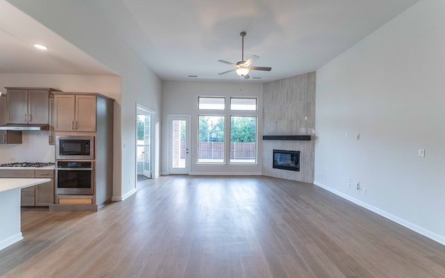 kitchen with appliances with stainless steel finishes, ceiling fan, hardwood / wood-style flooring, and a fireplace