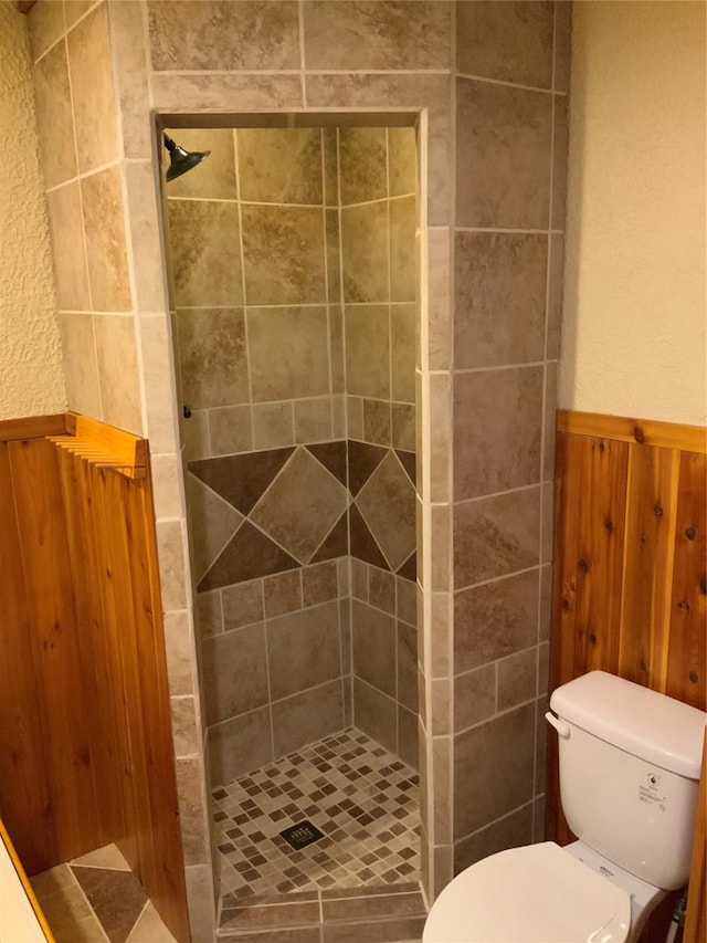 bathroom with a tile shower, wooden walls, and toilet