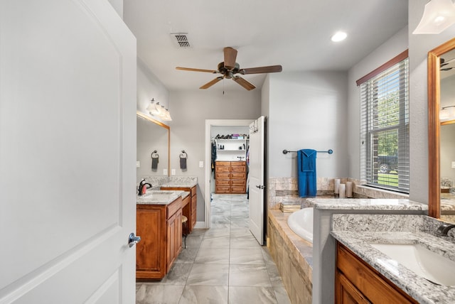 bathroom with tiled tub, ceiling fan, and vanity