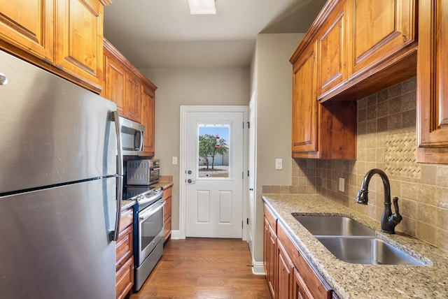 kitchen featuring sink, tasteful backsplash, light stone counters, appliances with stainless steel finishes, and light wood-type flooring