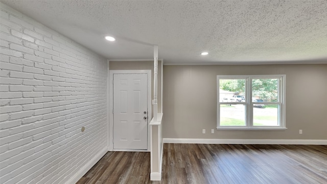 entryway featuring ornamental molding, brick wall, dark wood-type flooring, and a textured ceiling