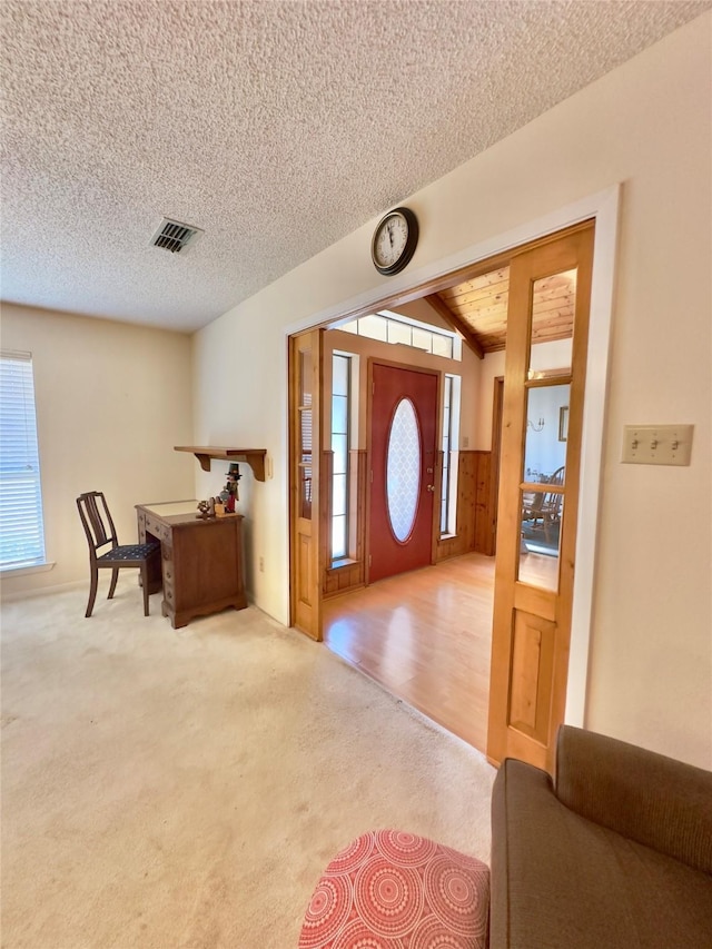 carpeted foyer featuring a textured ceiling and vaulted ceiling