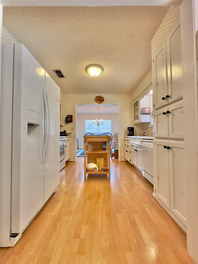 kitchen featuring hanging light fixtures, a chandelier, a textured ceiling, white appliances, and white cabinets