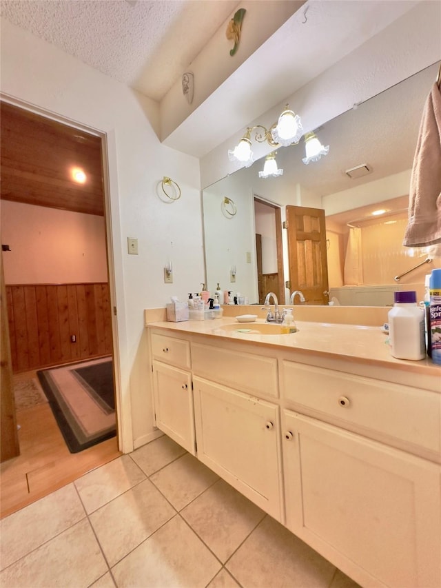 bathroom featuring tile patterned flooring, vanity, a textured ceiling, and wooden walls