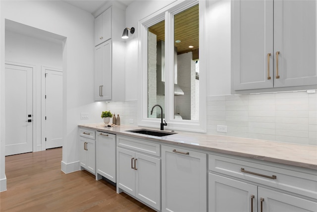 kitchen featuring white cabinetry, sink, light stone countertops, light hardwood / wood-style flooring, and white dishwasher