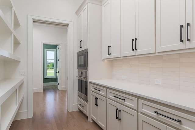 kitchen featuring white cabinets, oven, light stone counters, and light hardwood / wood-style flooring