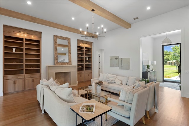 living room featuring beam ceiling, built in shelves, an inviting chandelier, a fireplace, and light wood-type flooring