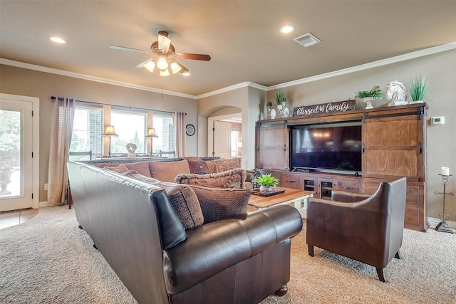 living area featuring arched walkways, light carpet, visible vents, a ceiling fan, and ornamental molding