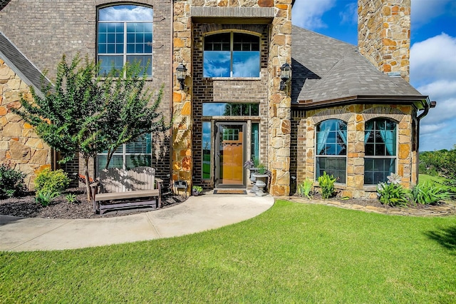 exterior space featuring stone siding, a chimney, roof with shingles, a yard, and brick siding