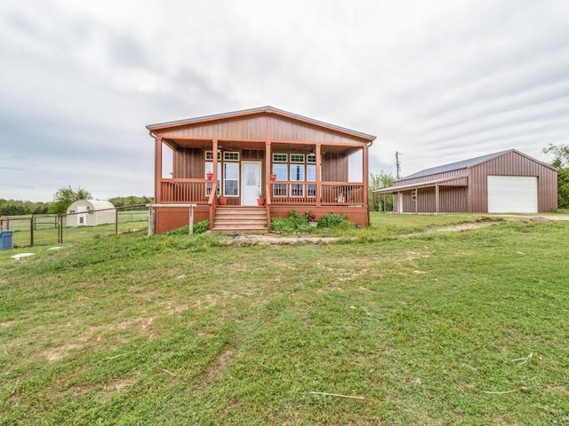 view of front of home featuring a garage, a porch, an outbuilding, and a front lawn