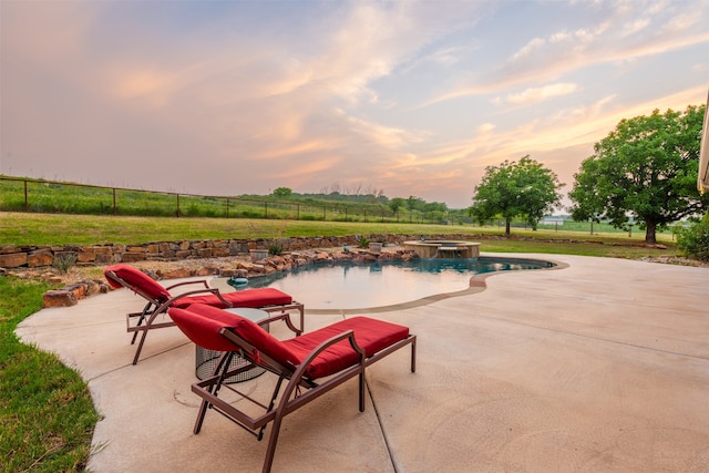 pool at dusk featuring a patio area, a yard, and an in ground hot tub