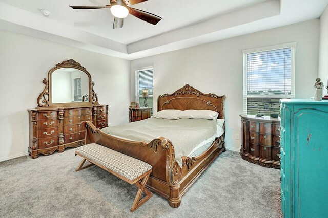 carpeted bedroom with a raised ceiling and ceiling fan