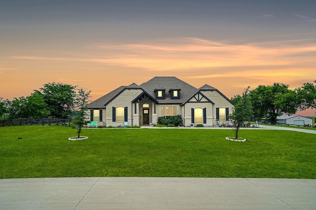 french country home featuring a shingled roof, a lawn, and fence