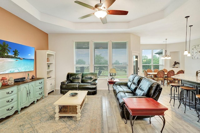 living room with a tray ceiling, plenty of natural light, and ceiling fan with notable chandelier