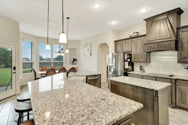 kitchen featuring stainless steel appliances, arched walkways, a sink, and an island with sink