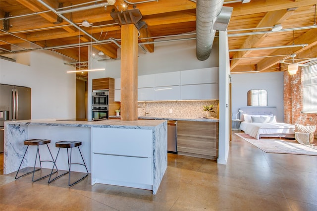 kitchen featuring stainless steel appliances, a breakfast bar, light stone counters, white cabinets, and backsplash