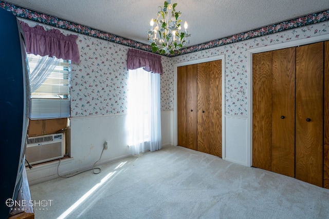 unfurnished bedroom with carpet flooring, a textured ceiling, cooling unit, a chandelier, and multiple closets