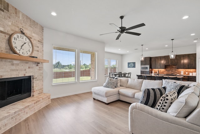 living room with a brick fireplace, ceiling fan, and light wood-type flooring