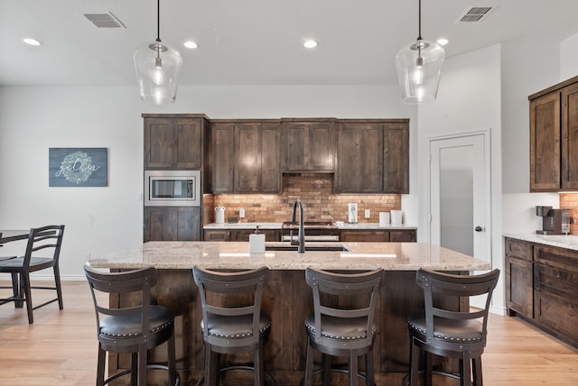 kitchen featuring dark brown cabinets, light hardwood / wood-style flooring, stainless steel microwave, and a kitchen island with sink