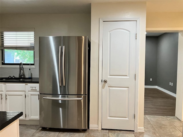 kitchen featuring light tile patterned flooring, sink, white cabinetry, stainless steel fridge, and decorative backsplash