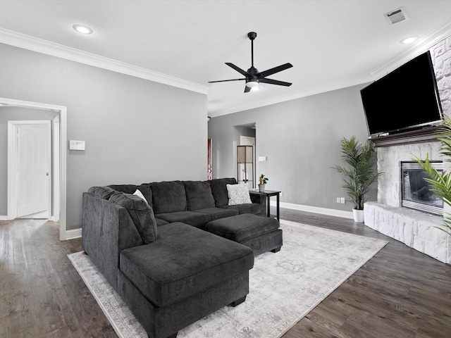 living room with crown molding, a fireplace, ceiling fan, and dark wood-type flooring