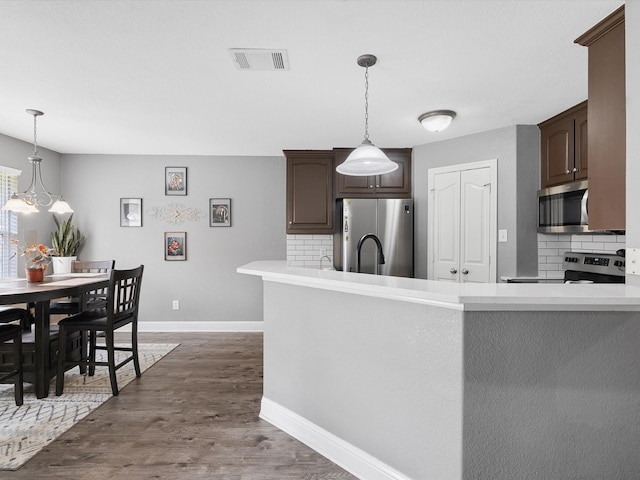 kitchen with pendant lighting, backsplash, an inviting chandelier, appliances with stainless steel finishes, and dark brown cabinets